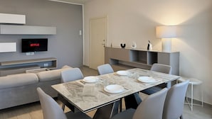 A modern living room with a sofa, a dining table set with plates and glasses, a TV displaying 'NETFLIX', and a lamp on a side table. - Suite Patrizia - Appartamento nel Cuore di Modena (Modena)
