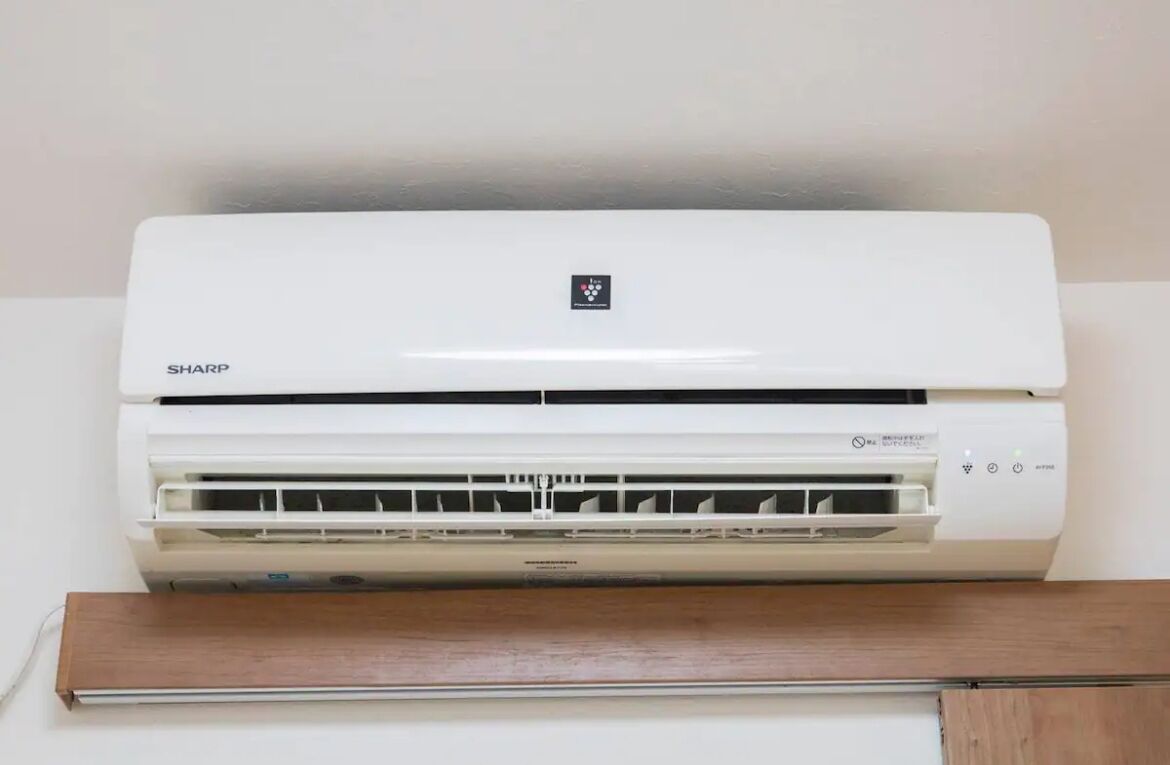 A white air conditioning unit with a control panel and a wooden shelf below it.
