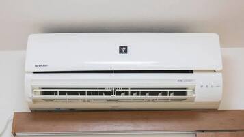 A white air conditioning unit with a control panel and a wooden shelf below it.