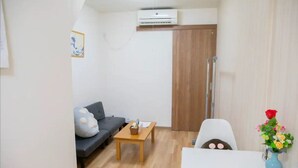 A compact living space with a sofa, a small table, a white chair, a wooden door, and a wall-mounted air conditioner. - 樺音閣 One private house, Near the benten station, USJ and aquarium, and free Wi-Fi (大阪市港区弁天5丁目)