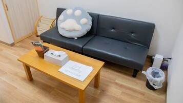 Une pièce avec un canapé en cuir noir, une table basse en bois, une poubelle blanche et un petit sac poubelle blanc posé sur le sol.