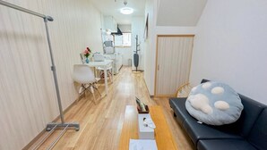 A narrow hallway with a wooden floor, a black sofa with a polka-dotted pillow, a white chair, a small table with a vase of flowers, and a metal rack. - 樺音閣 One private house, Near the benten station, USJ and aquarium, and free Wi-Fi (大阪市港区弁天5丁目)