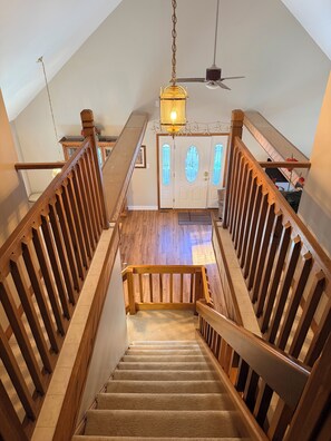 A wooden staircase with a carpeted landing, a chandelier, and a ceiling fan.