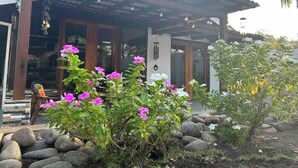 Una casa con tejado de baldosas, un porche y un jardín con plantas en flor.