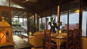 A dining area with a wooden table and chairs, a potted plant, and a candle on a stand.