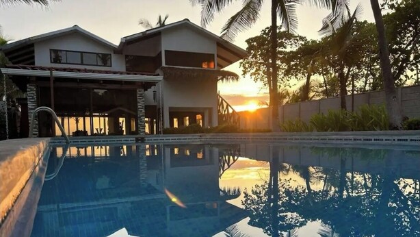 Un área de piscina moderna con vista despejada a un edificio de dos pisos y palmeras.