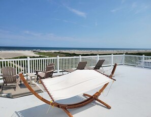 A deck with a hammock, chairs, and a view of the beach. - Water's Edge Ocean Resort (Wildwood Crest)