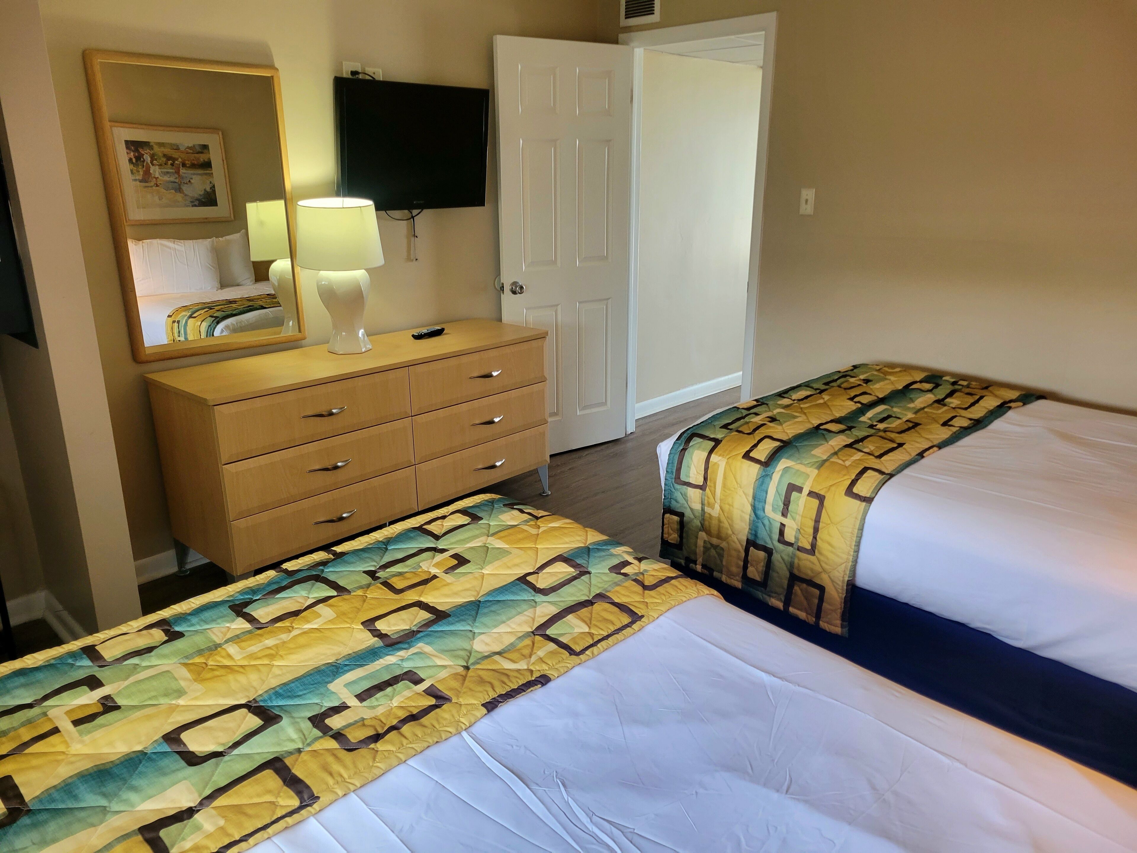 A hotel room with two beds, a dresser, a TV, and a door.