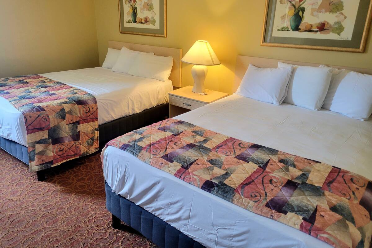 A hotel room with two beds, each with a quilted bedspread and white linens. There are two bedside tables with lamps, and the walls are adorned with framed floral artwork.
