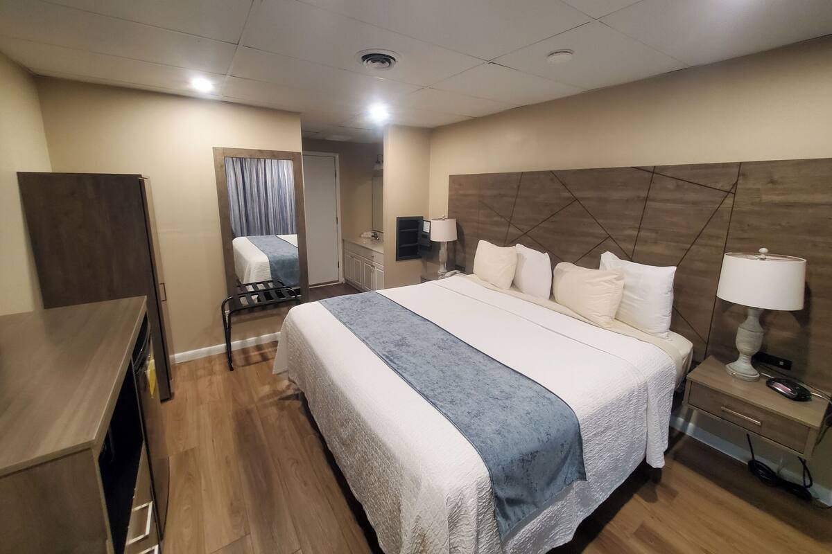 A hotel room with a large bed, bedside tables with lamps, a wooden headboard, a wardrobe, and a mirror.