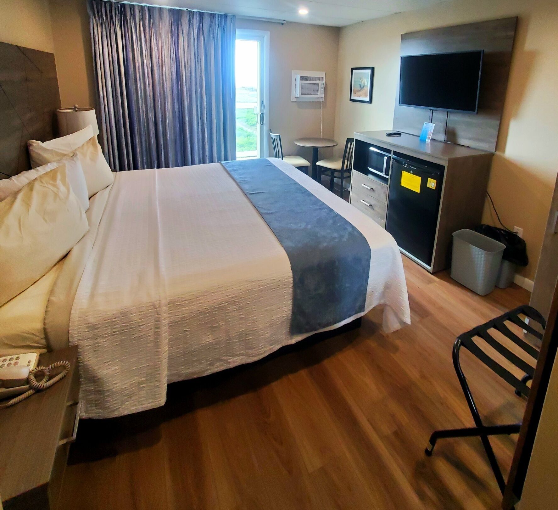 A hotel room with a large bed, a desk with a computer, a TV, and a window with curtains.