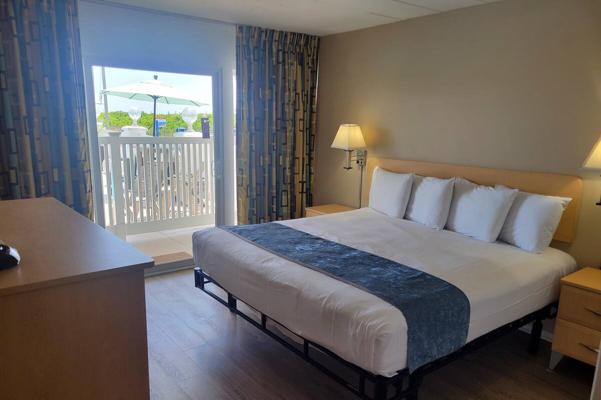 A hotel room with a large bed, a desk, a nightstand, and a view of the outside balcony.