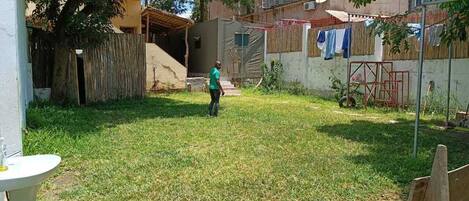 Un césped con una persona de pie, una valla de madera y un edificio al fondo.