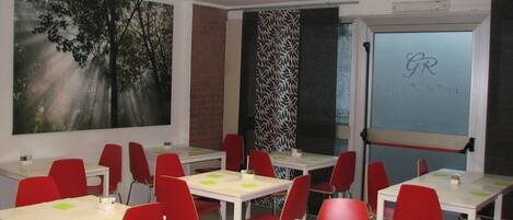 A classroom with red chairs and white tables, a large forest mural, and a projector screen with a logo.