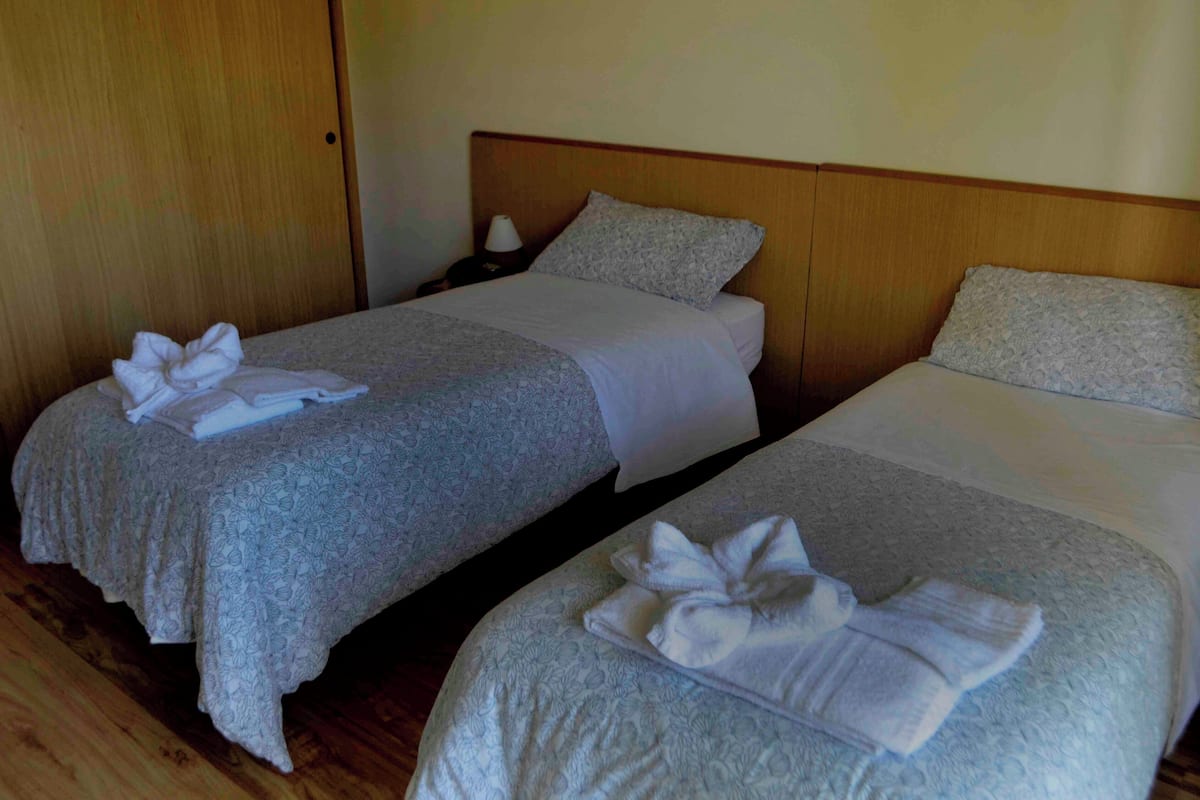 Two single beds with white linens and towels, wooden headboards, and a wooden floor.