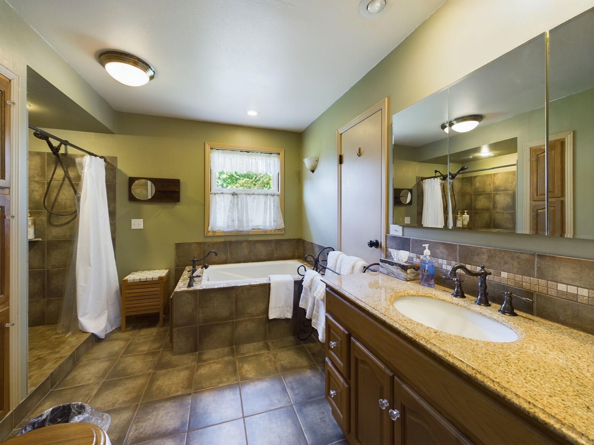 A bathroom with a bathtub, two sinks, a large mirror, and a window with a curtain.