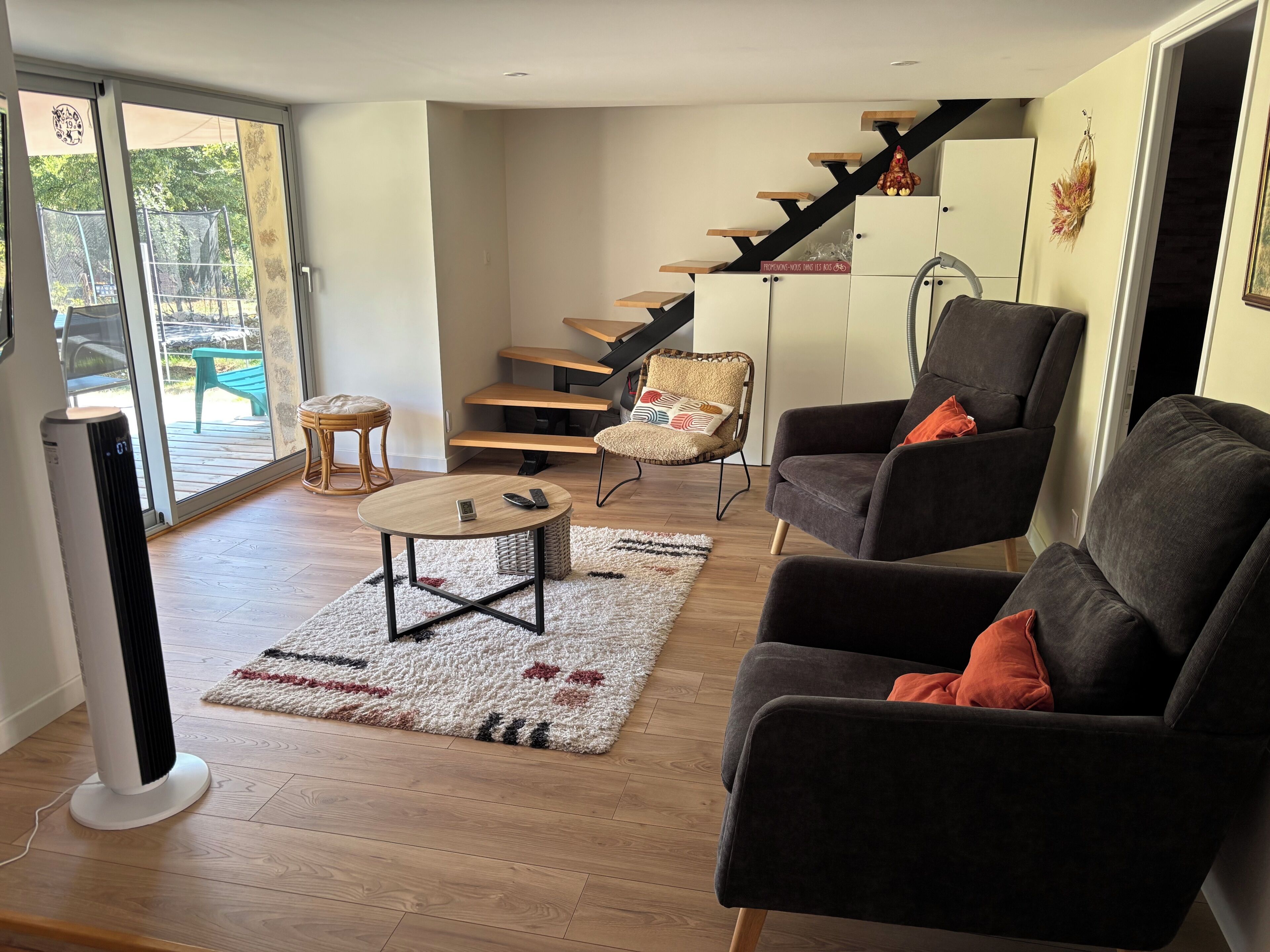 A modern living room with a sofa, armchair, and a coffee table. There is a staircase with wooden steps and a chair with a cushion.