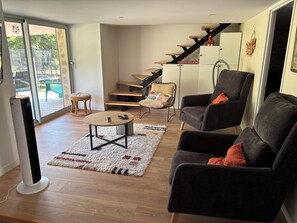 A modern living room with a sofa, armchair, and a coffee table. There is a staircase with wooden steps and a chair with a cushion.