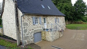 Une maison en pierre avec une allée en gravier et un escalier en métal menant à une porte.