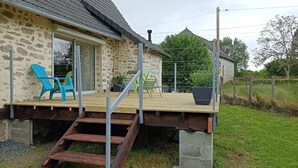 Un bâtiment en pierre avec une terrasse en bois, une chaise bleue et un pot de fleurs.