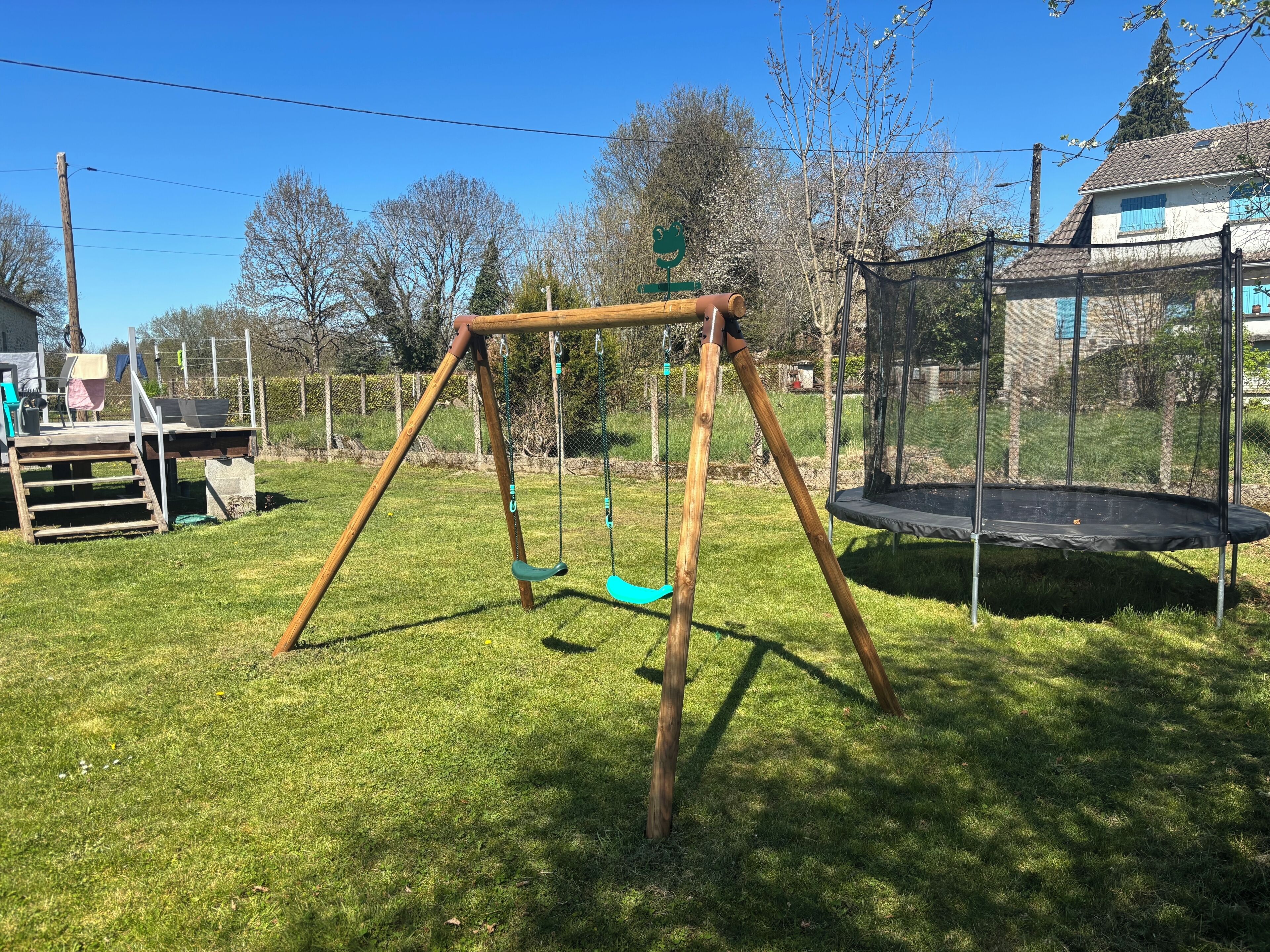 Ein Holzschaukel und ein Trampolin in einem Garten.