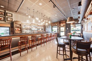 A bar area with wooden chairs and tables, a bar counter with bottles and glasses, and pendant lighting. - Exclusive Group Hotel Buyout | Private Bar + Event Space (Louisville)