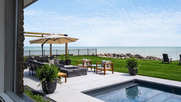 Een zwembadgedeelte met uitzicht op de oceaan, buitentafels en -stoelen, en een pergola.