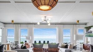 Un vaste salon doté d’une grande fenêtre donnant sur la mer, et aménagé avec des canapés, des fauteuils et une table ronde en verre.