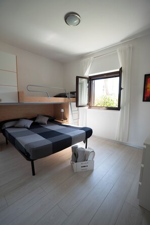 Ein Schlafzimmer mit Etagenbett, Nachttisch, Lampe und einem Fenster mit Vorhängen.