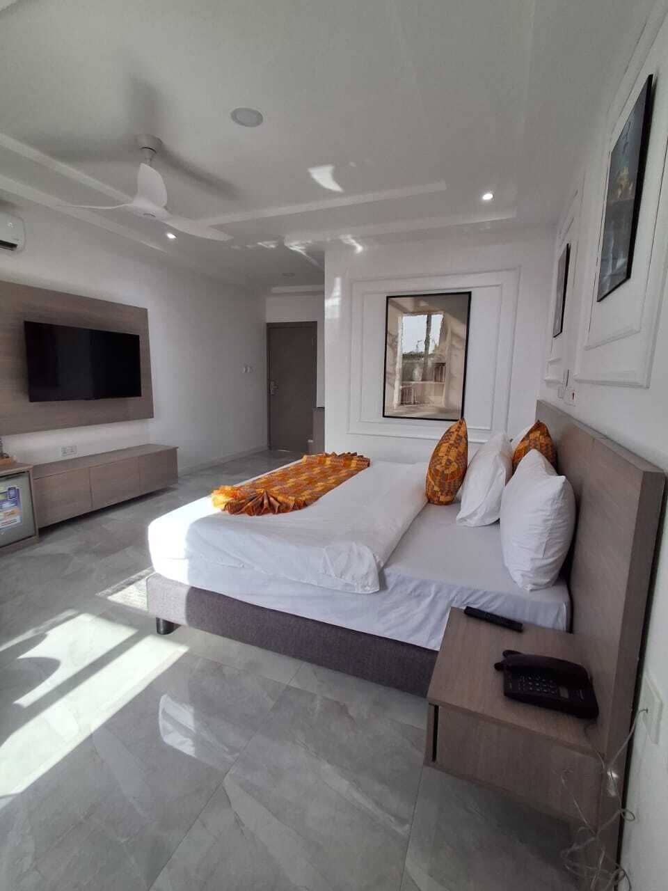 A modern hotel room with a bed, a TV, a bedside table, and a window.