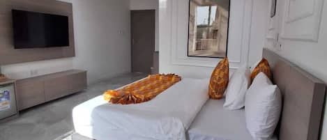 A modern hotel room with a bed, a TV, a bedside table, and a window.