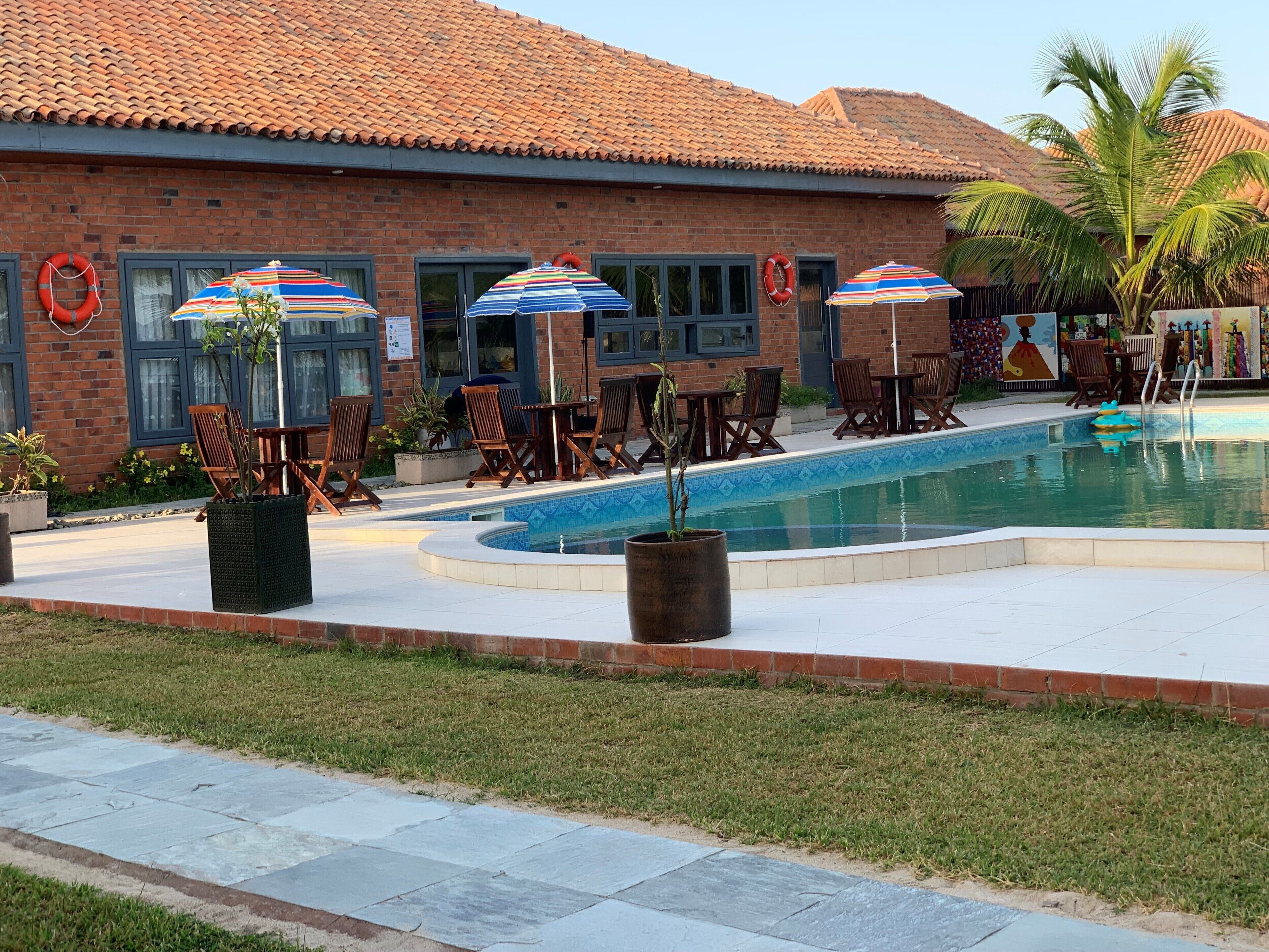 Zona junto a la piscina con un edificio de ladrillo, sillas de descanso y sombrillas.