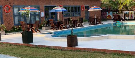 Zona junto a la piscina con un edificio de ladrillo, sillas de descanso y sombrillas.