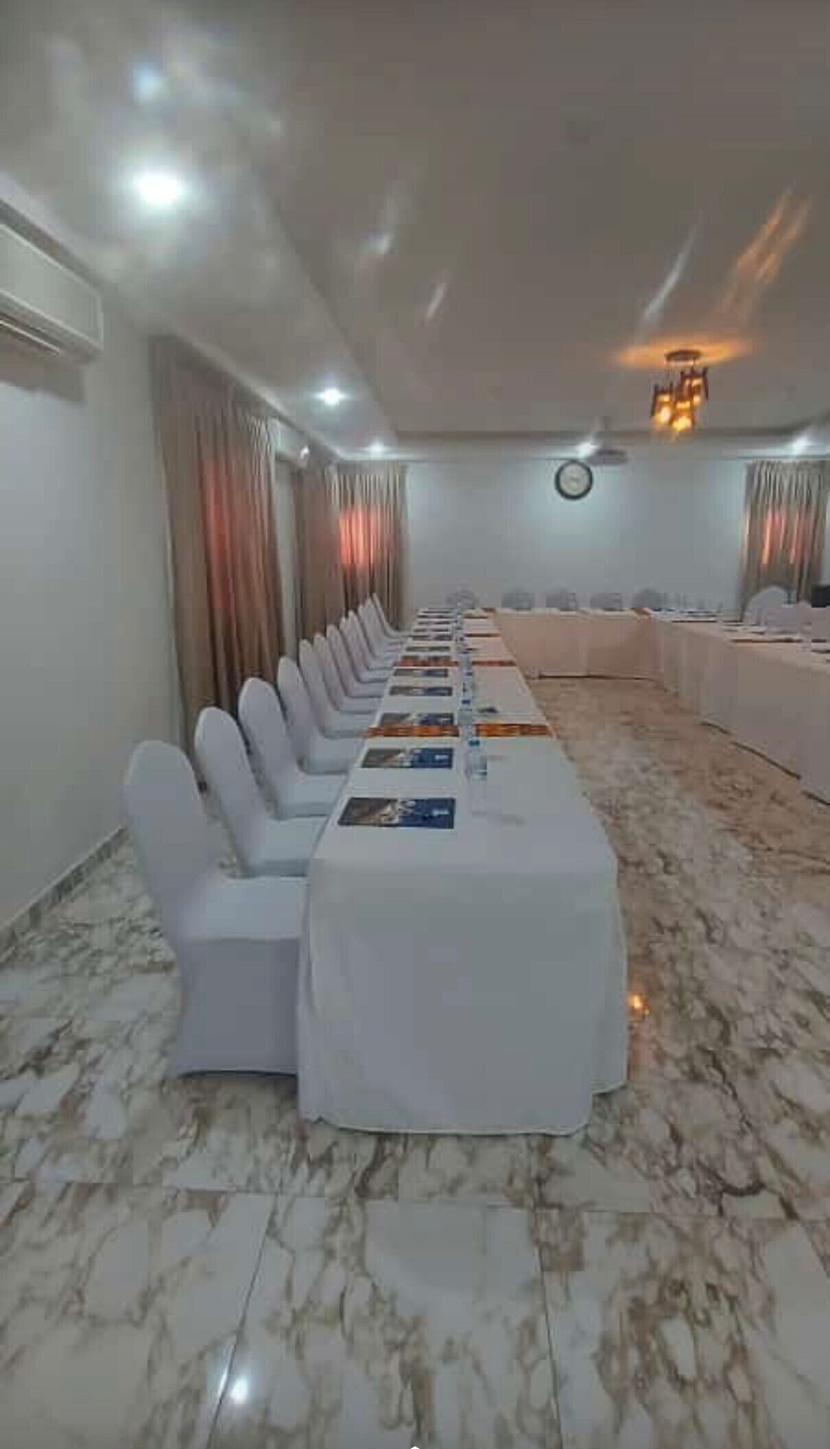 Une salle de conférence avec une longue table, des chaises blanches et un sol en marbre.