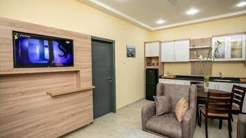Una sala de estar moderna con un televisor de pantalla plana montado en una pared de madera, un sofá gris con cojines, una mesa de centro de mármol y un ventilador de techo.