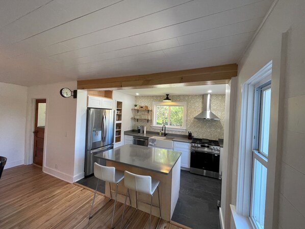 A modern kitchen with a central island, stainless steel appliances, and a window providing natural light. - Ironton Stone Cottage, walk to Lake Charlevoix beach. (Charlevoix)