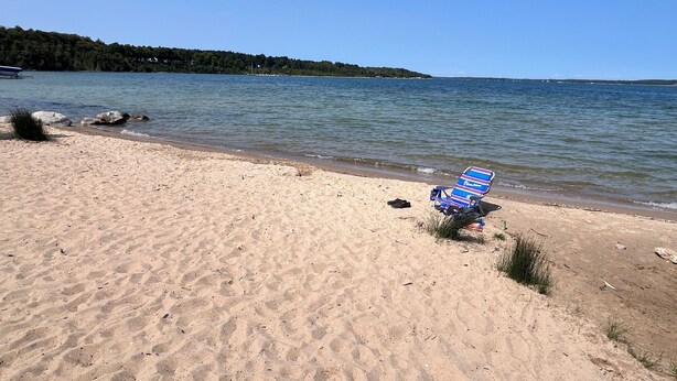 A beach with a single beach chair and a pair of shoes on the sand.