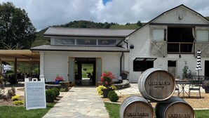A winery entrance with a stone pathway leading to the door, surrounded by potted plants and pumpkins.