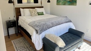 A neatly arranged bedroom with a bed, bedside tables, a bench, a painting, and a window with curtains.