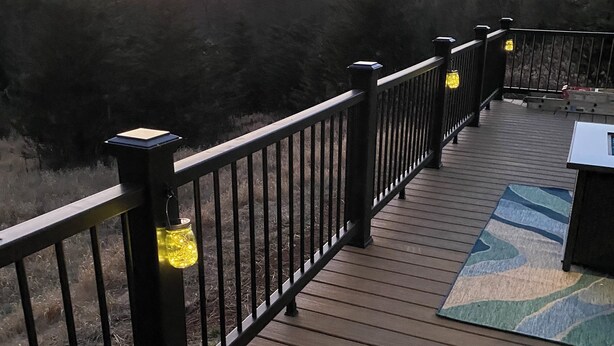A wooden deck with railings and a rug, overlooking a forested area.