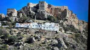 A castle on a rocky hill with modern buildings in the foreground.