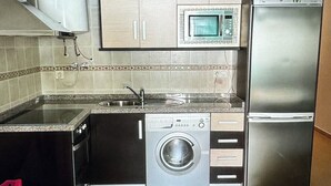 A compact kitchen with a microwave, refrigerator, washing machine, and a sink.