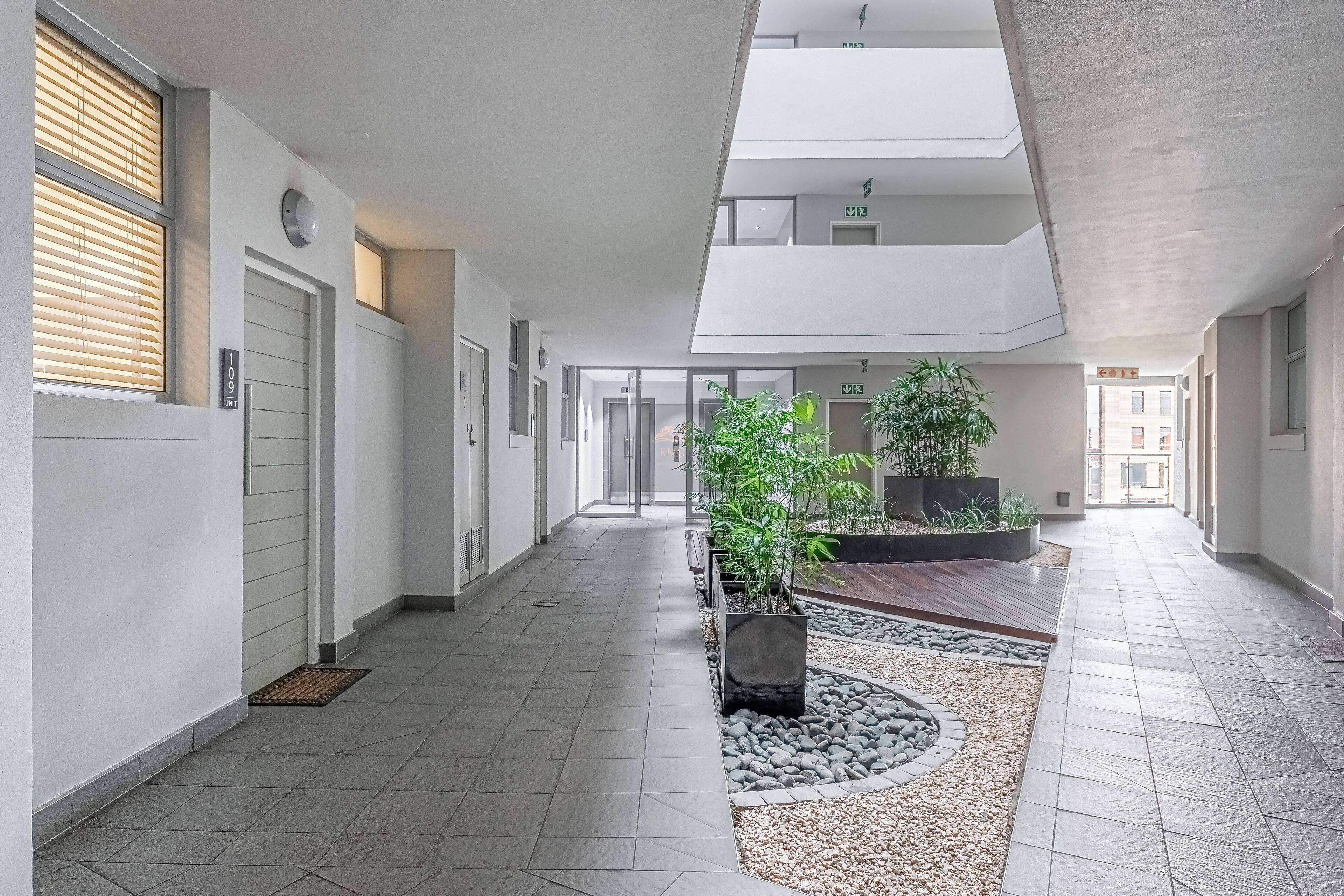 Een moderne hotelgang met dakraam, potplanten en een betegelde vloer.
