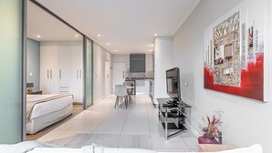 A modern hotel room with a bed, a TV, a desk, and a dining area. - KMG Apartments at The Apex on Smuts  (Johannesburg)