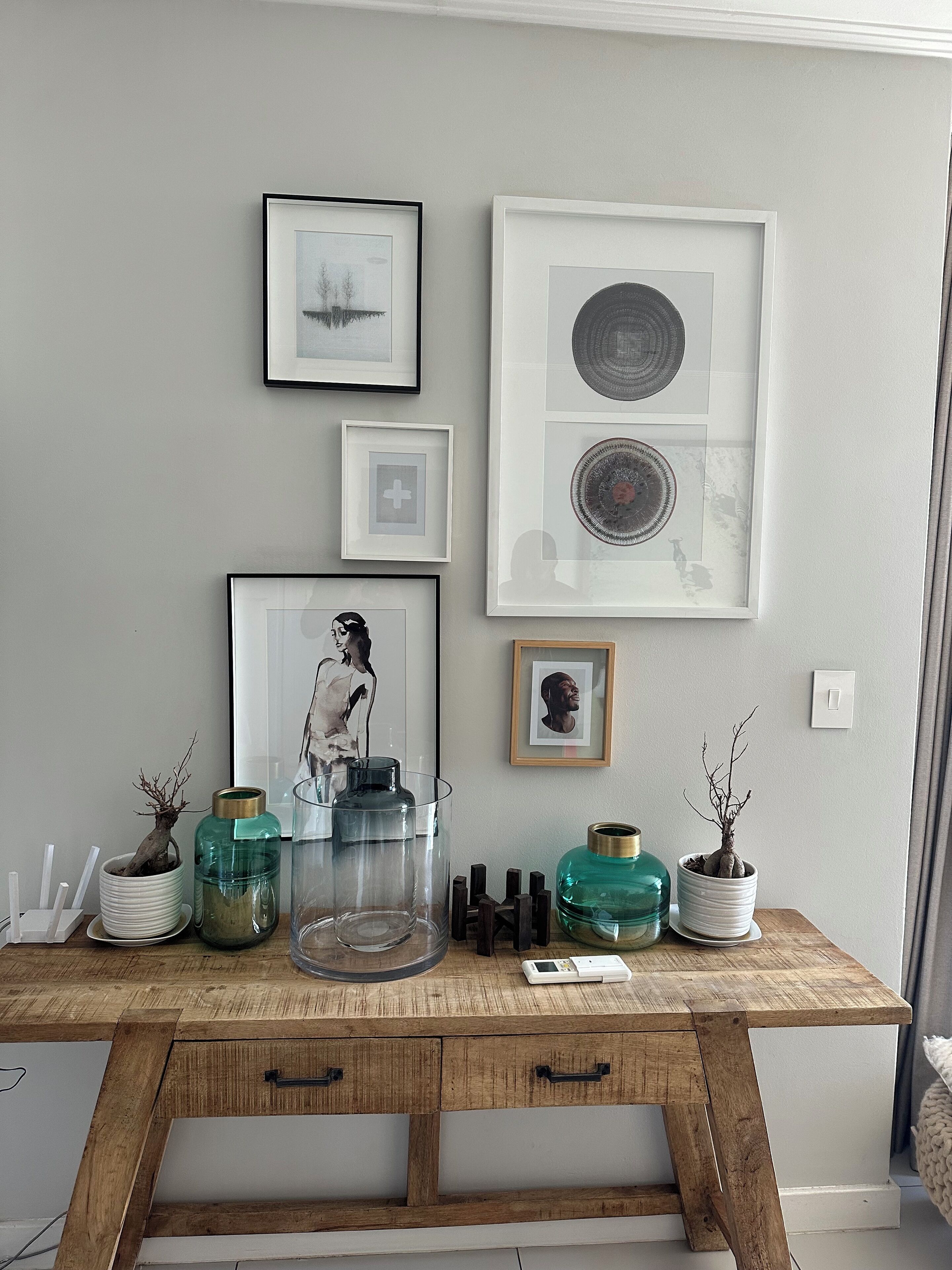 A wooden desk with framed artwork, a potted plant, and a glass vase.