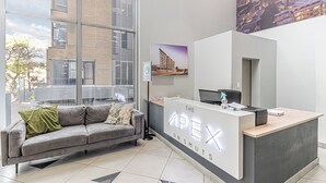 A modern reception desk with a cityscape view, a grey sofa, and a framed picture on the wall. - KMG Apartments at The Apex on Smuts  (Johannesburg)