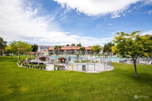 A hotel with a swimming pool, a covered patio, and a well-maintained lawn.