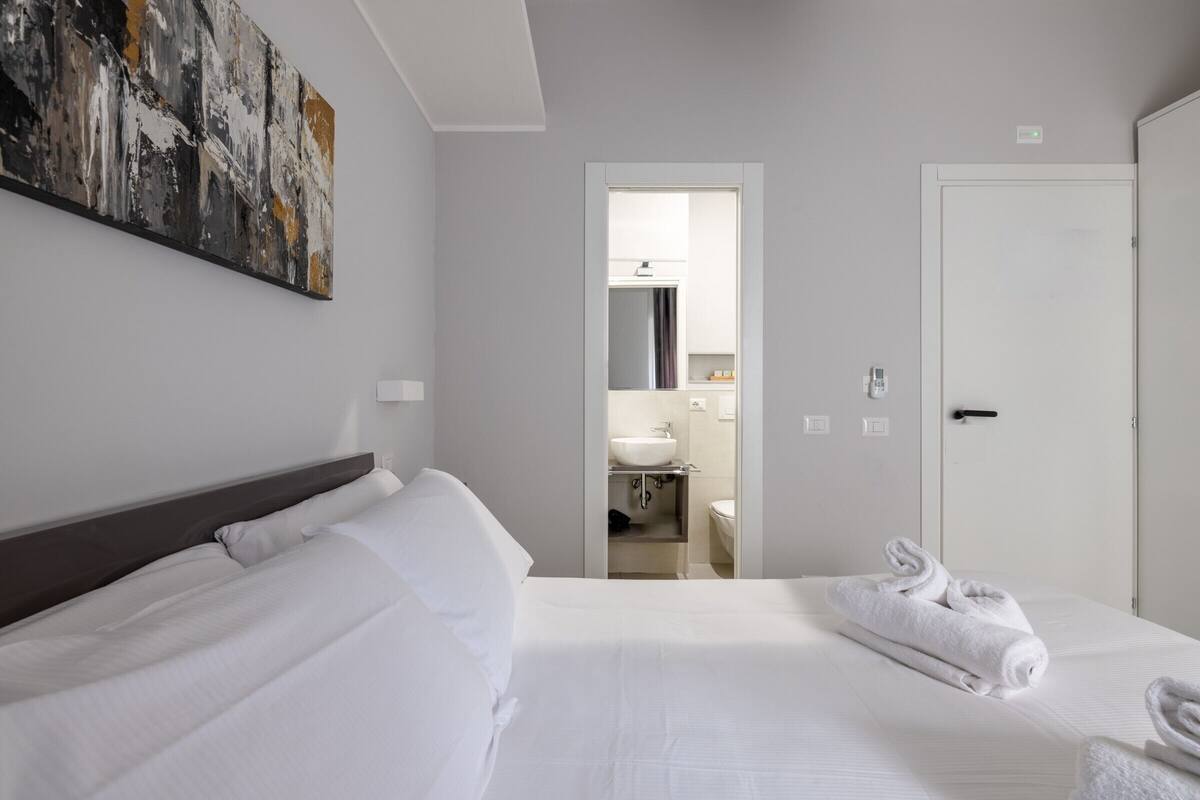 A hotel room with a large bed, a painting on the wall, and a bathroom visible through an open door.
