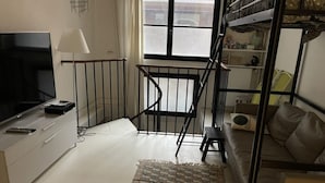 A room with a TV, a sofa, a small table, a window, and a staircase. - Duplexe Paris 6eme (Paris)