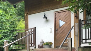 Eine Holztreppe führt zu einer Tür mit Klingel und Laterne an der Wand.